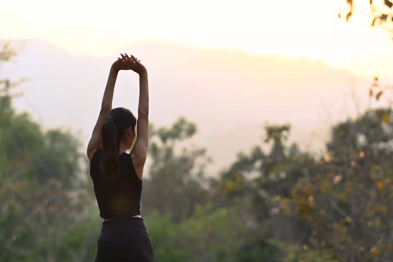 Shot of young woman stretching in the park Woman in activewear stretching arms outdoors at sunrise